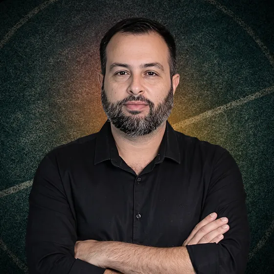 Luis Esteves, de braços cruzados, com camisa preta, sobre um fundo de gramado escuro